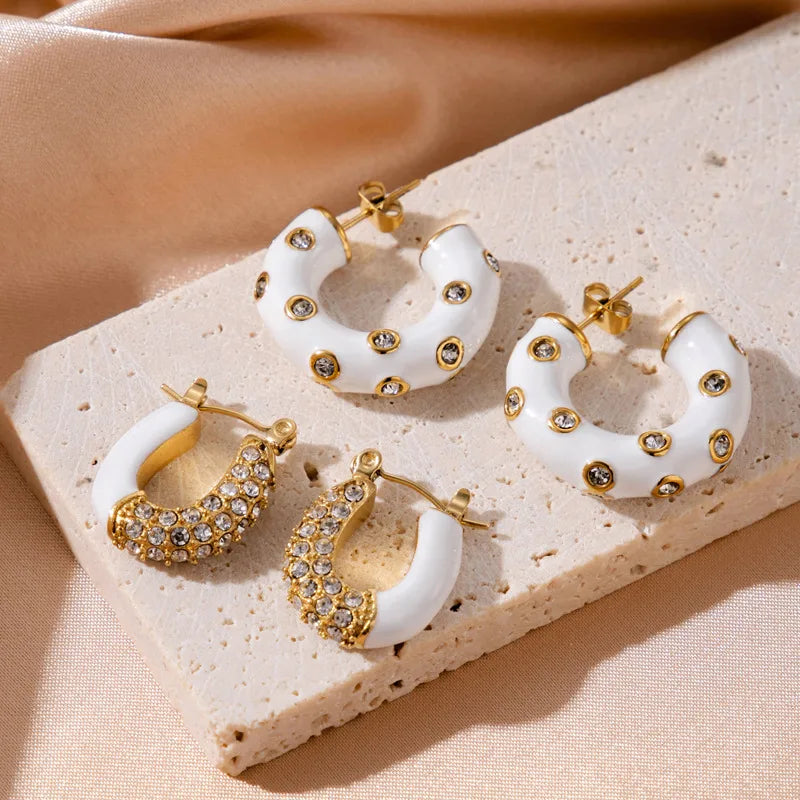 Set of white hoop earrings with gold accents on a beige surface